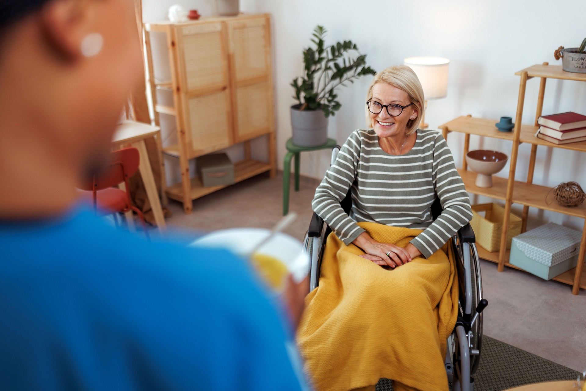 Female nurse brining hot soup bowl to mature woman in wheelchair